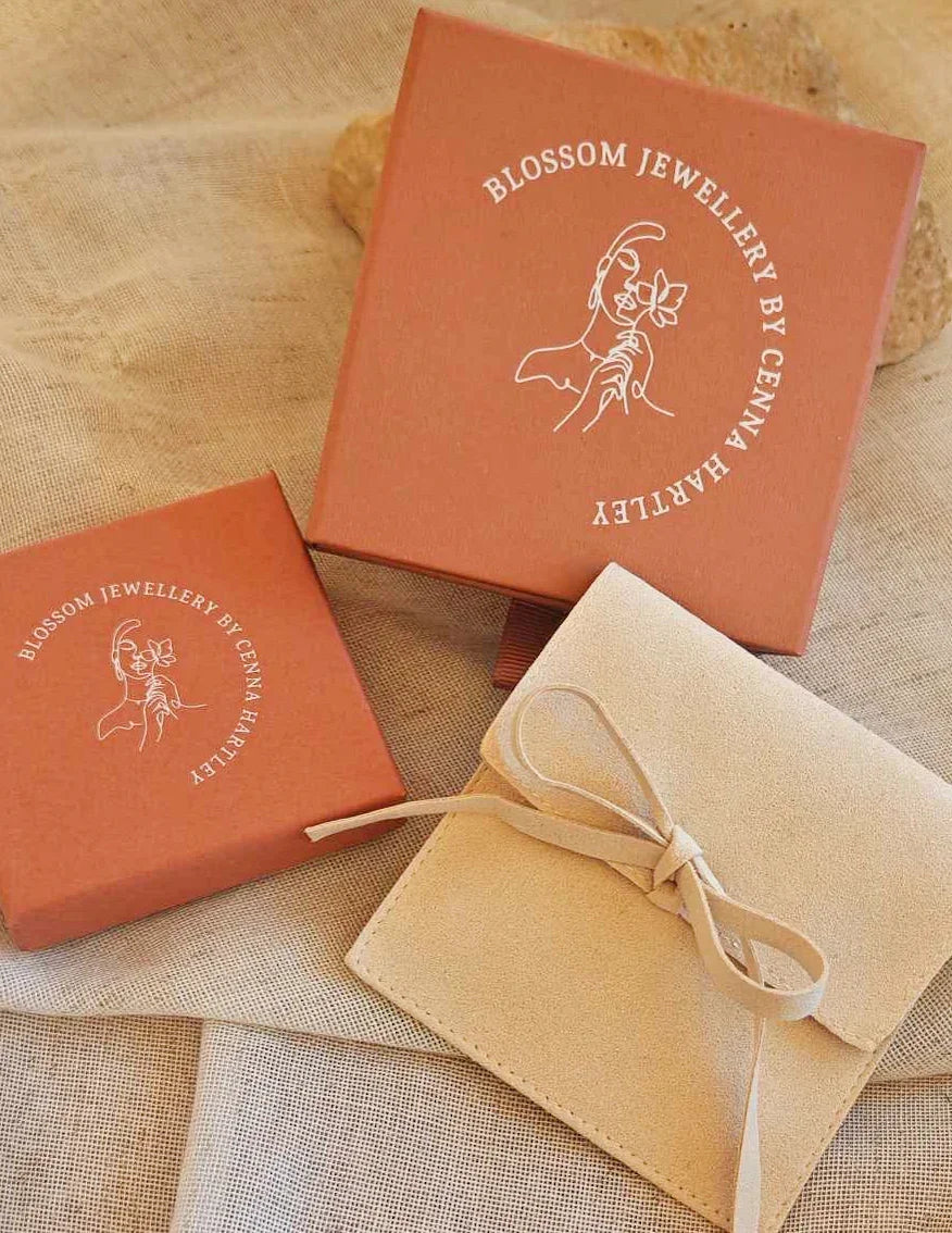 Rust-colored jewelry gift boxes and a beige suede pouch on linen fabric, elegant packaging.