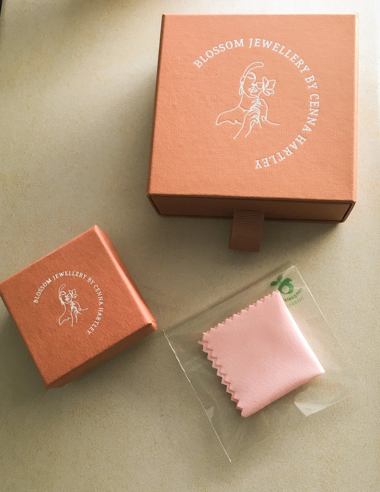Jewelry packaging boxes with illustration and pink polishing cloth on beige background
