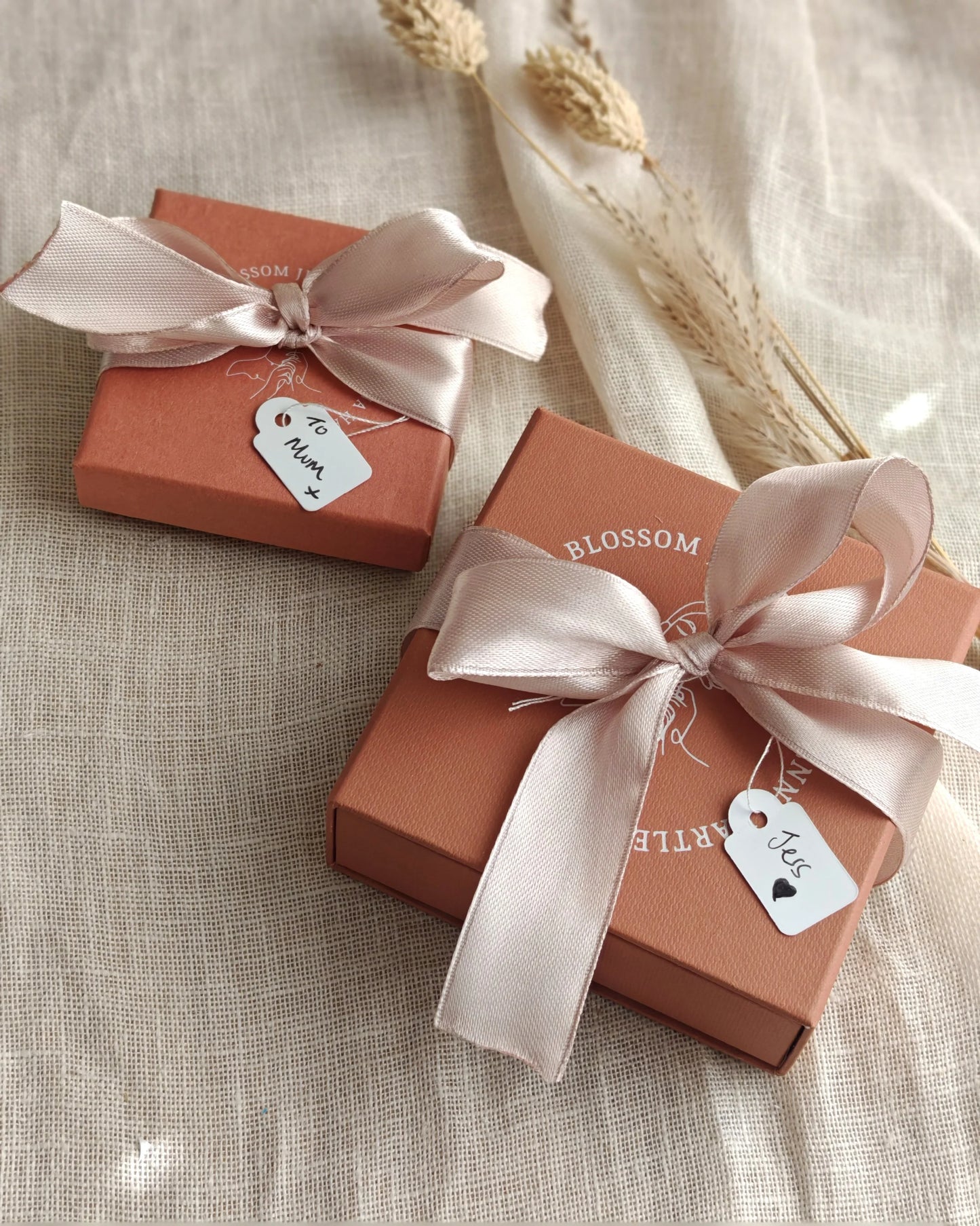 Two peach jewelry gift boxes with satin ribbons and gift tags on beige fabric background