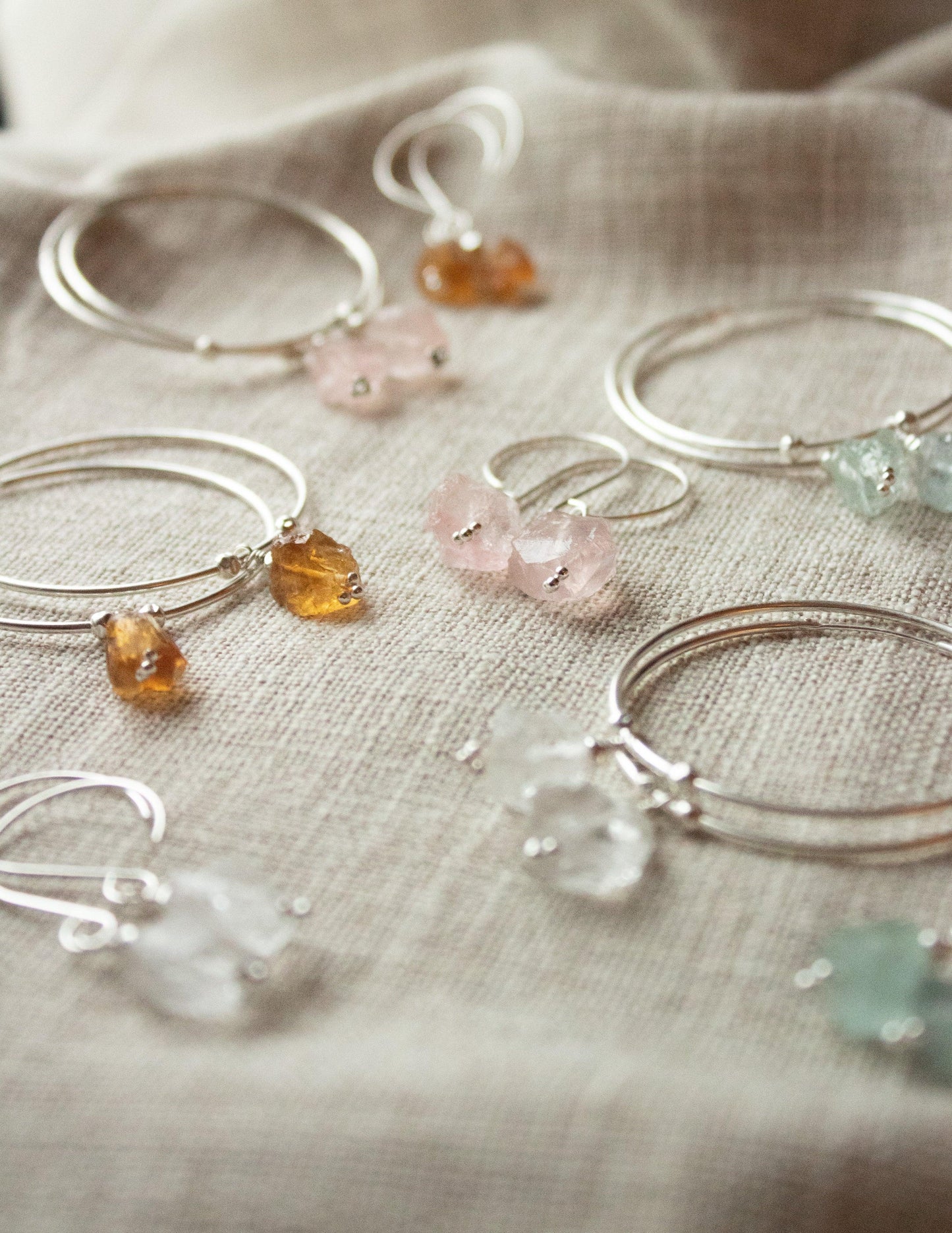 Handmade sterling silver bracelets and earrings with colorful gemstone charms on linen fabric