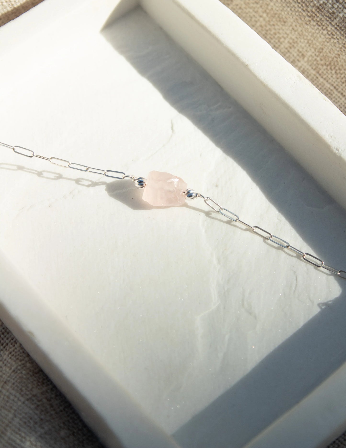 Sterling silver chain bracelet with raw rose quartz gemstone on a textured tray
