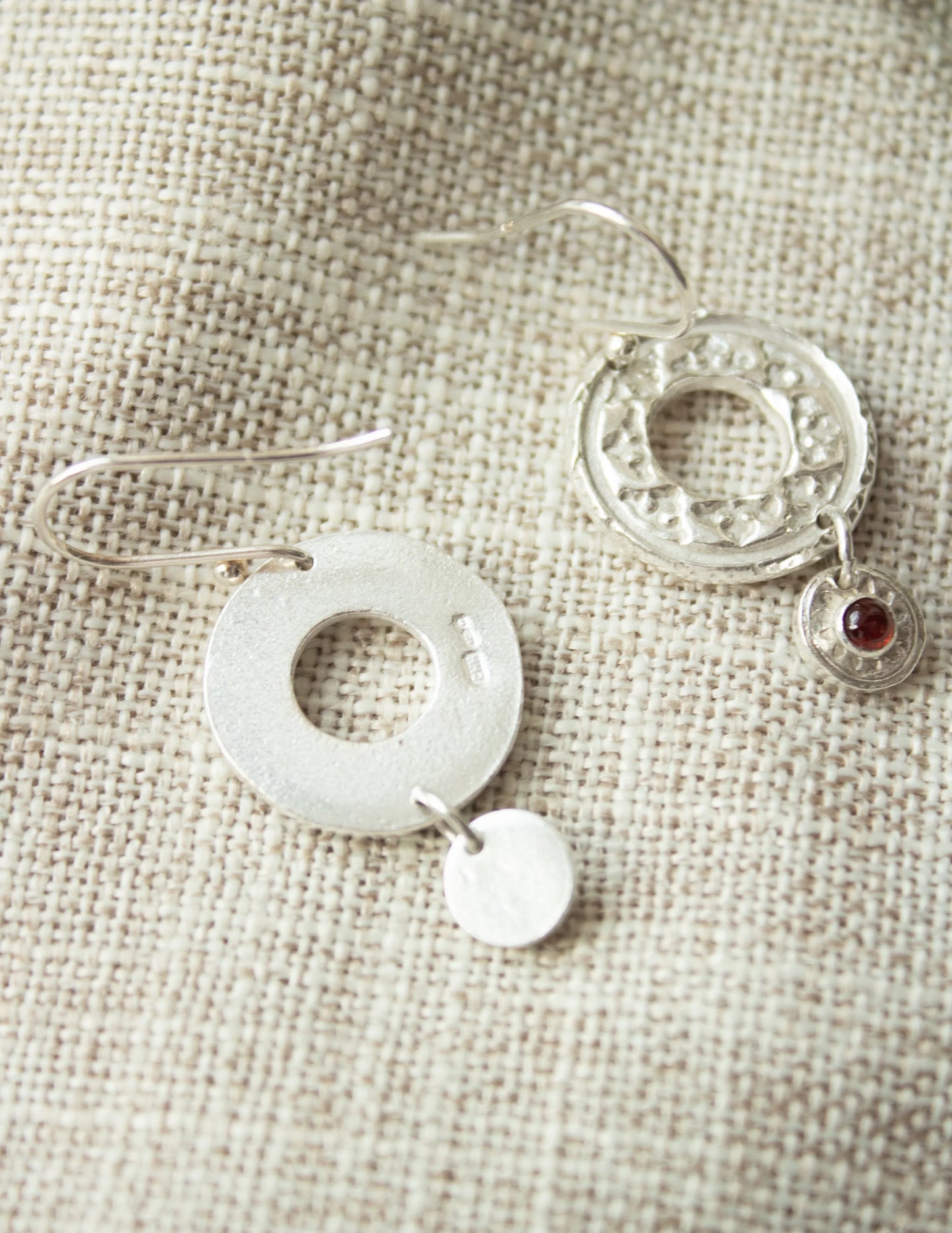 Handmade sterling silver dangle earrings with circular and gemstone accents on fabric