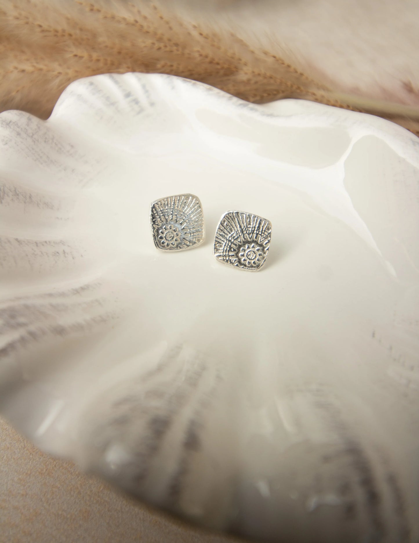 Handmade sterling silver textured stud earrings on a ceramic dish