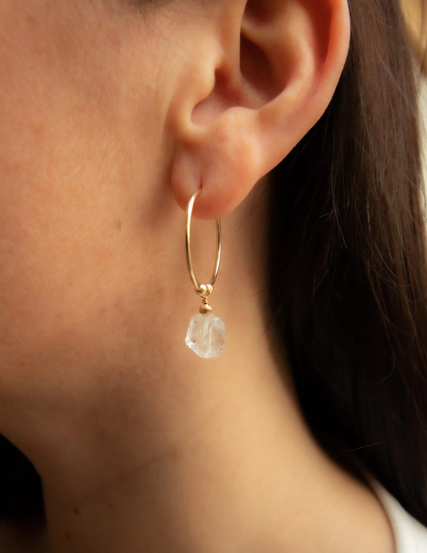 Gold hoop earring with raw gemstone dangle on ear, handmade jewelry close-up