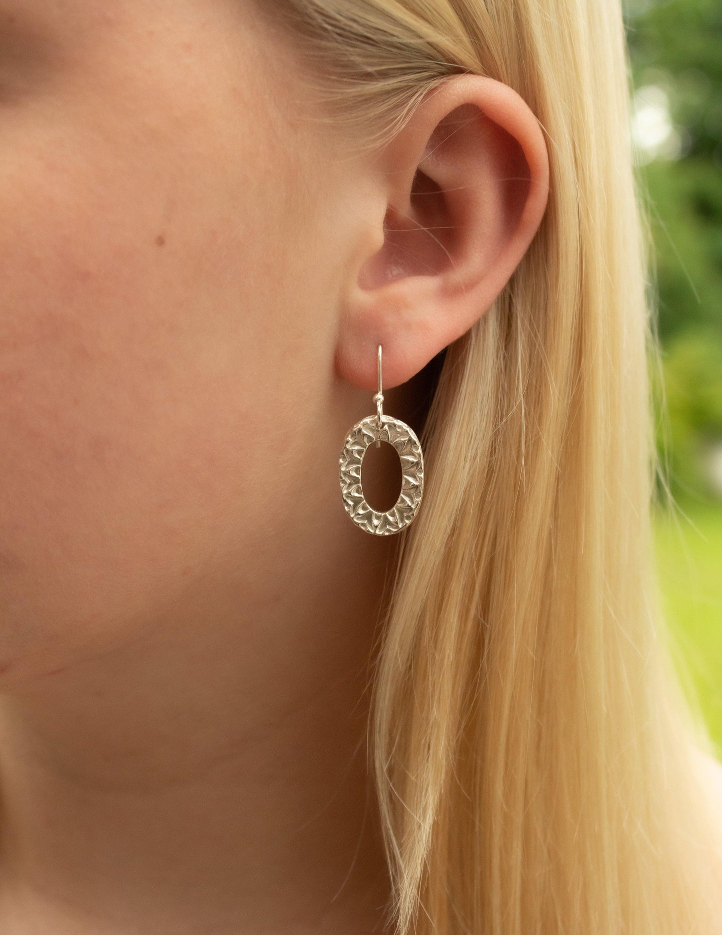 Hammered sterling silver oval dangle earring worn on ear, handmade jewelry closeup