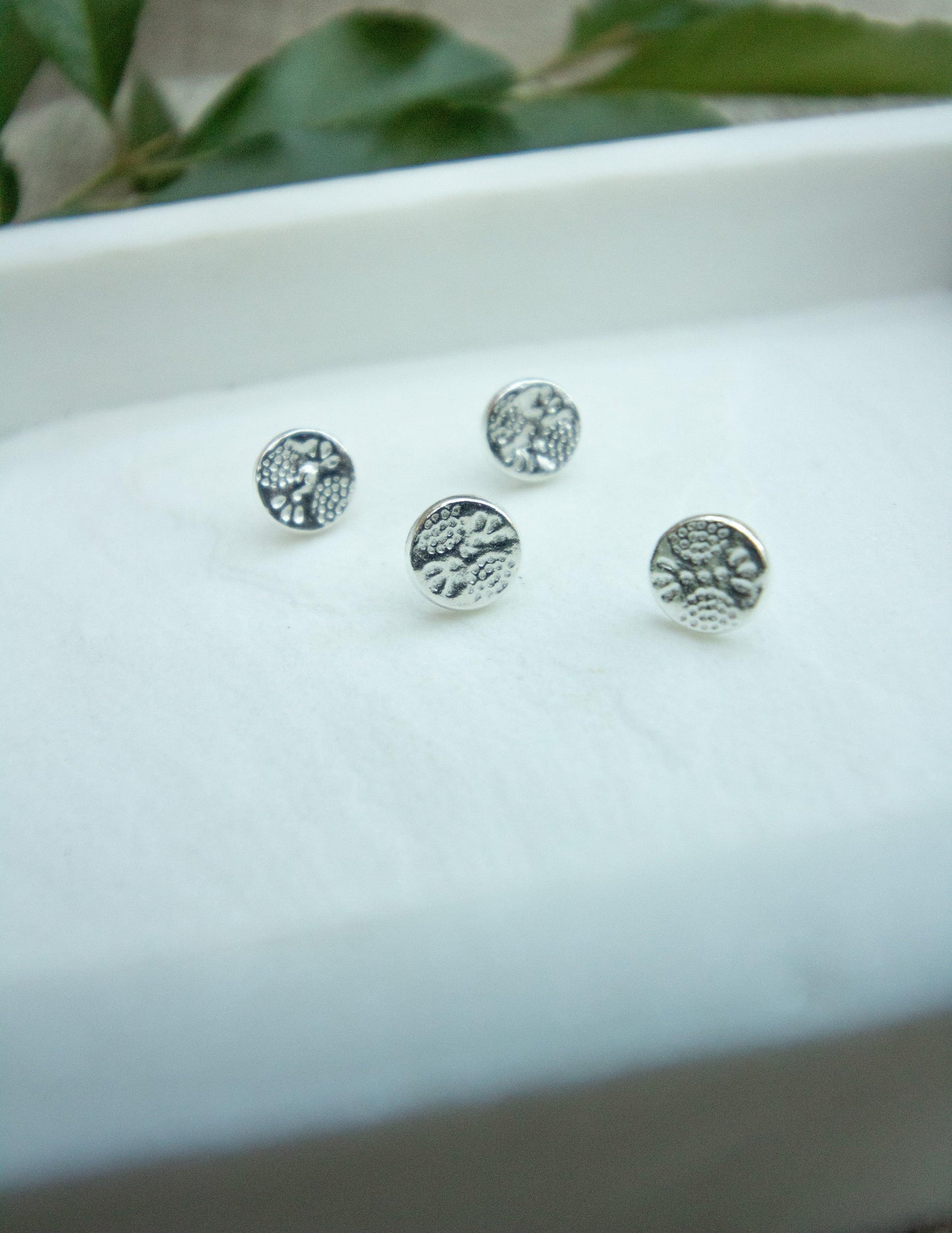 Sterling silver round stud earrings with textured botanical design on white display