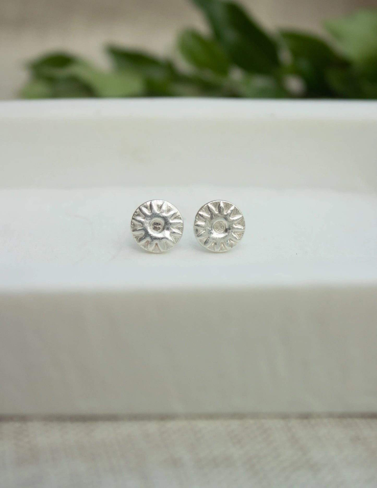 Textured sterling silver sunburst stud earrings on a white display