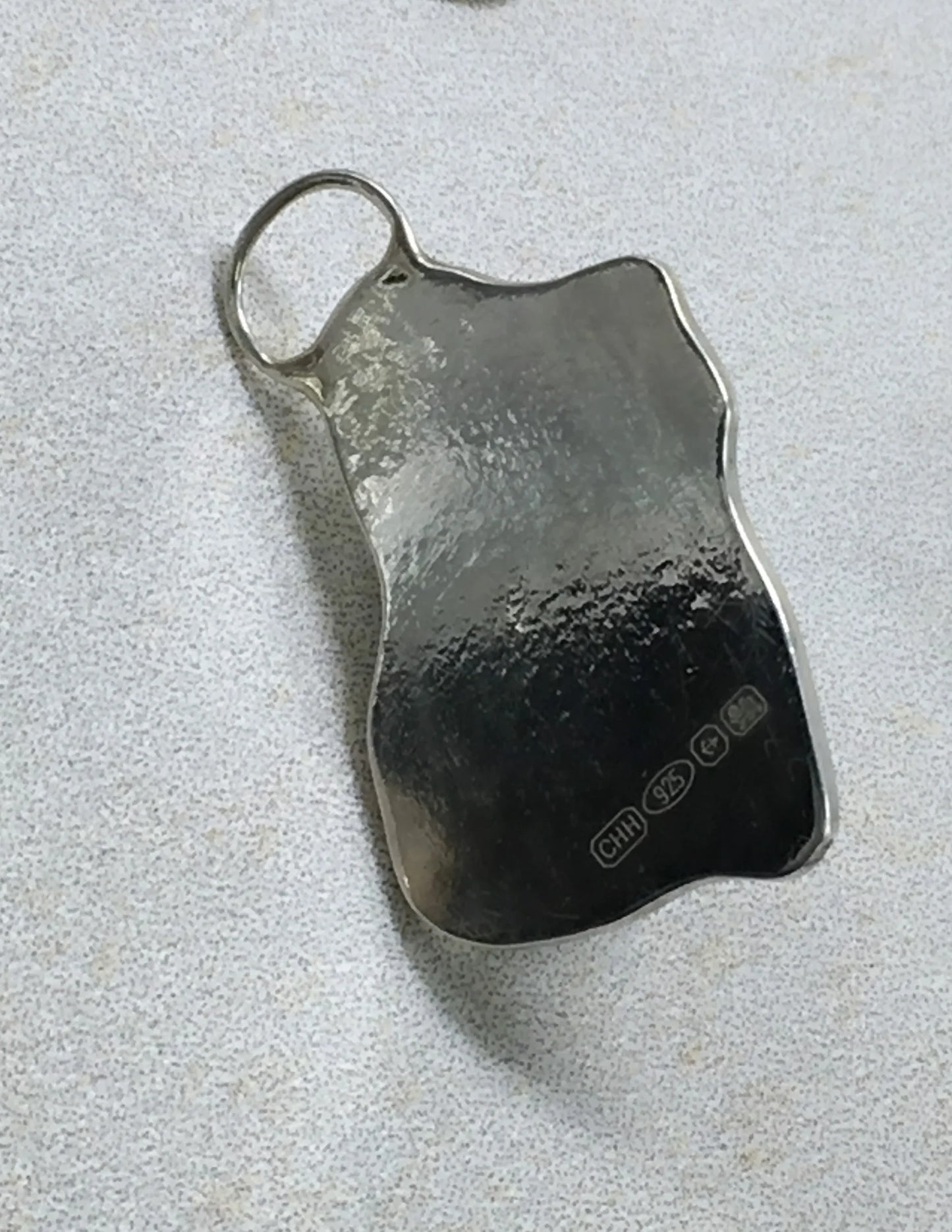 Textured sterling silver jewelry pendant with stamped 925 hallmark on a light surface