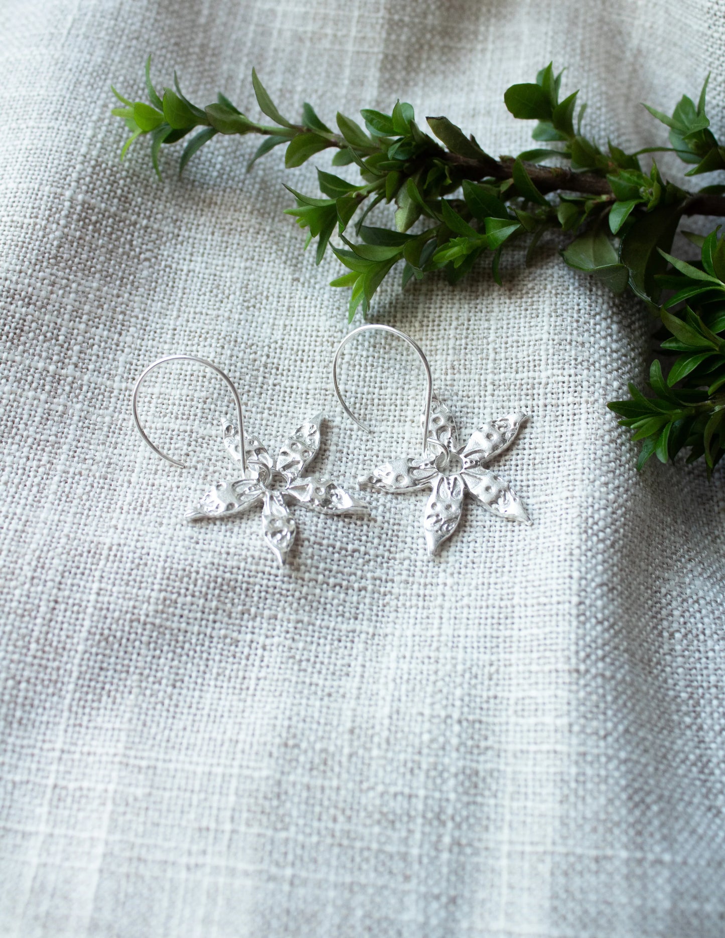 Handmade sterling silver floral earrings on linen with green foliage