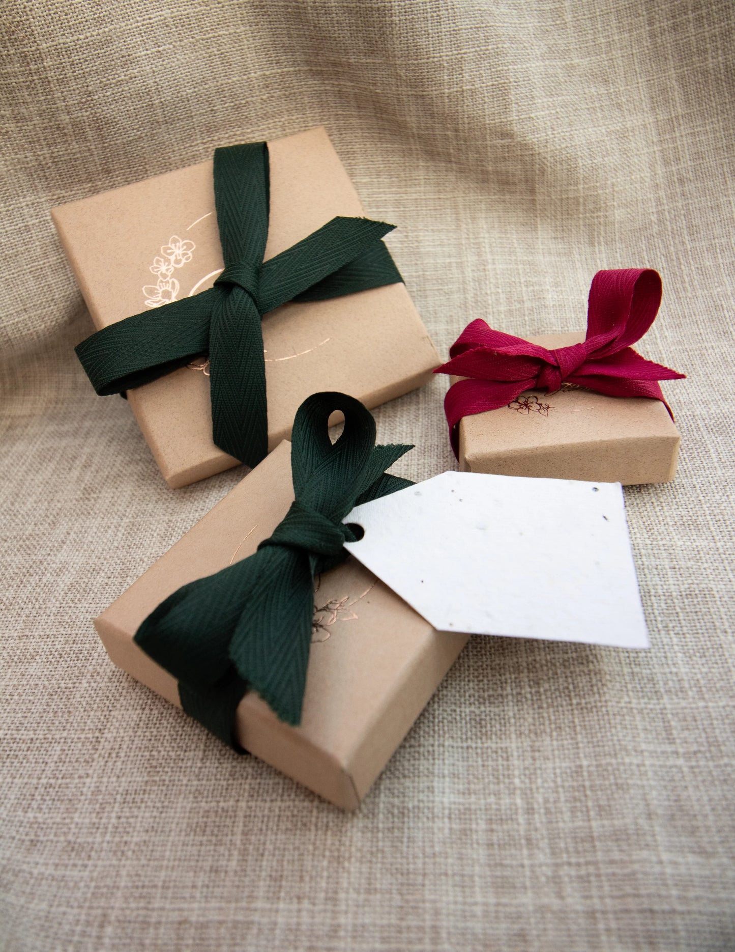 Gift boxes with green and red fabric ribbons on linen, perfect for jewelry packaging.
