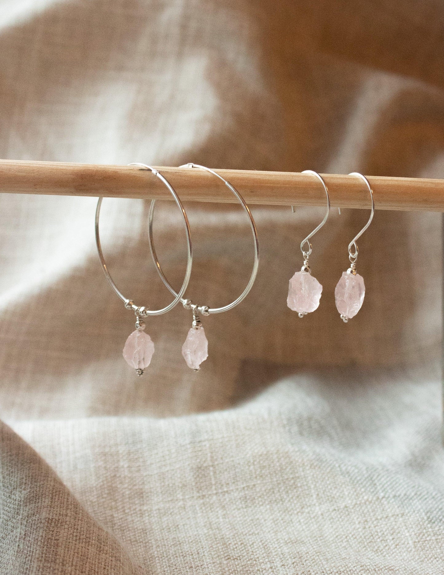 Sterling silver hoop and drop earrings with raw pink gemstones on neutral fabric background