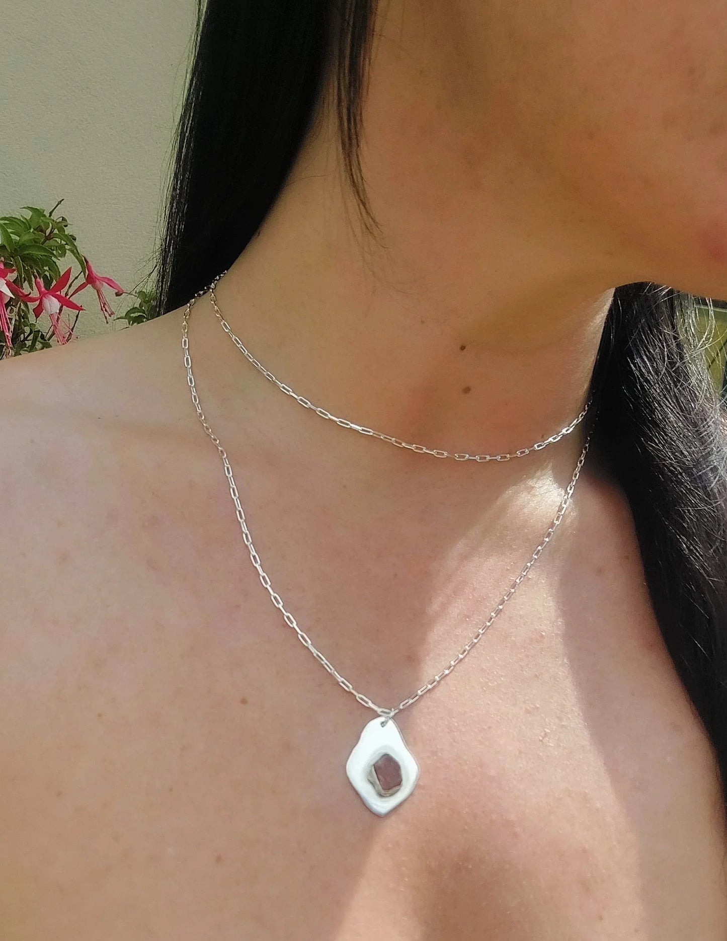 Woman wearing two sterling silver necklaces, one with an organic-shaped pendant