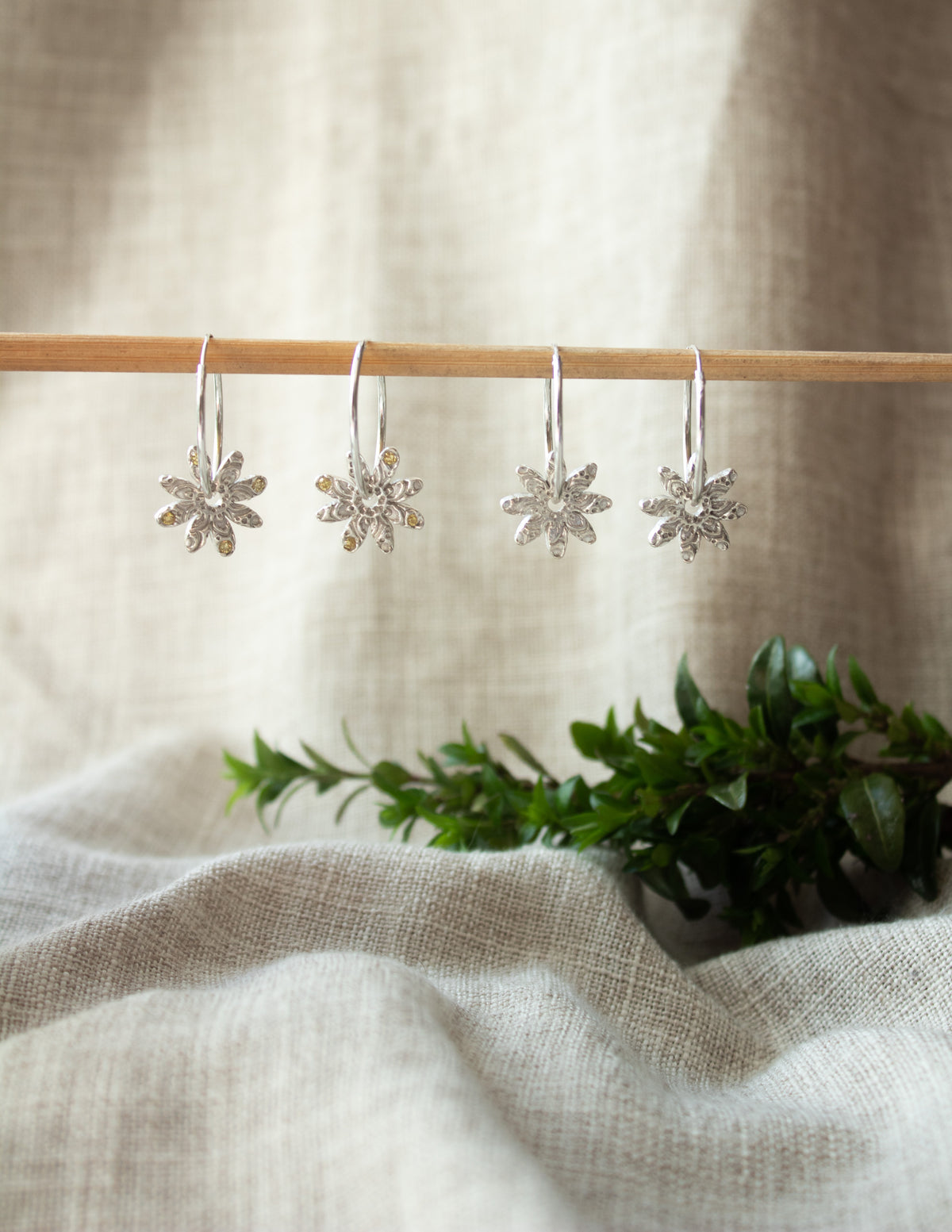 Sterling silver floral earrings with textured petals hanging on a rod, neutral fabric background.