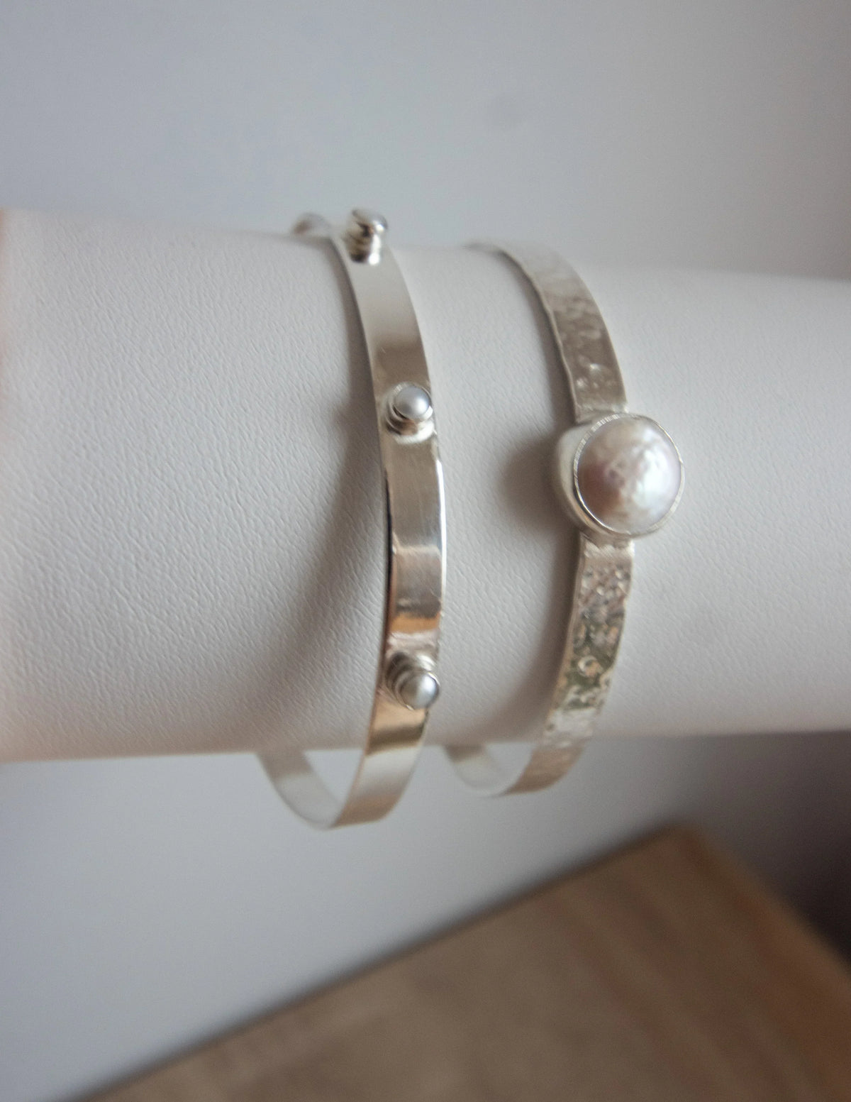 Sterling silver bangles with hammered texture and pearl gemstone accents on display stand