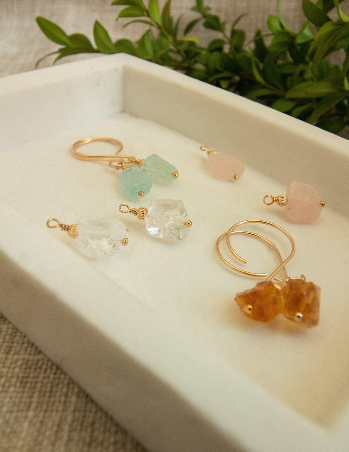 Handmade gemstone earrings with gold-filled hooks in a white tray, assorted colors