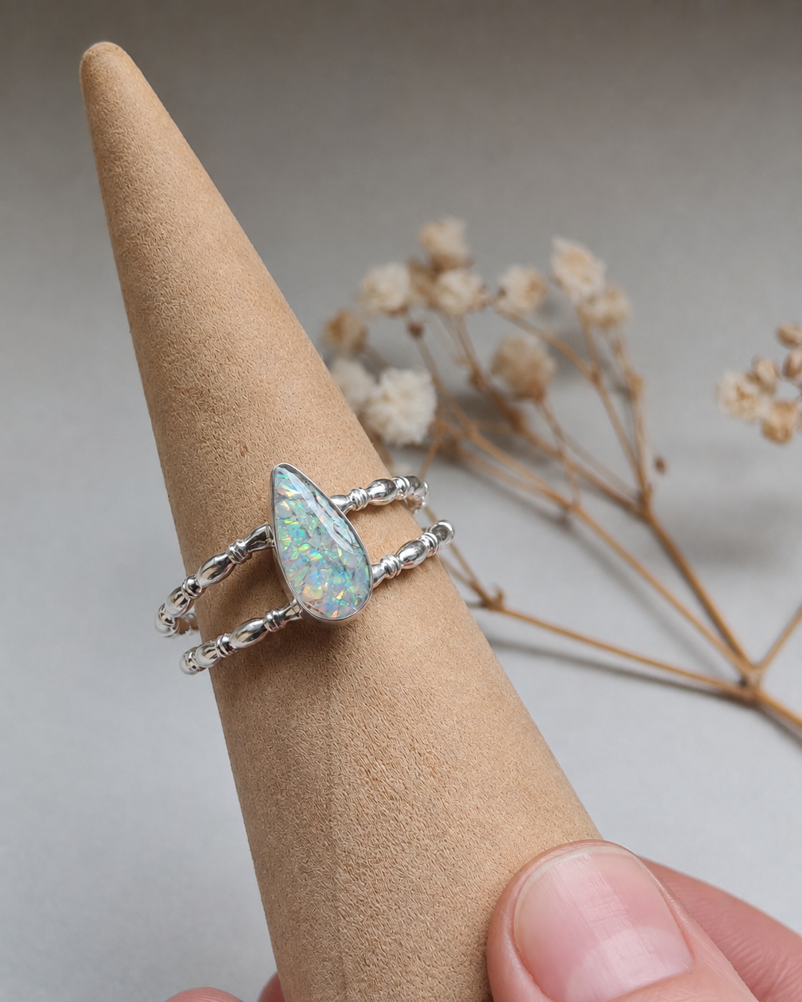 Hand holding gift box with a gemstone ring, pink ribbon, and floral decor