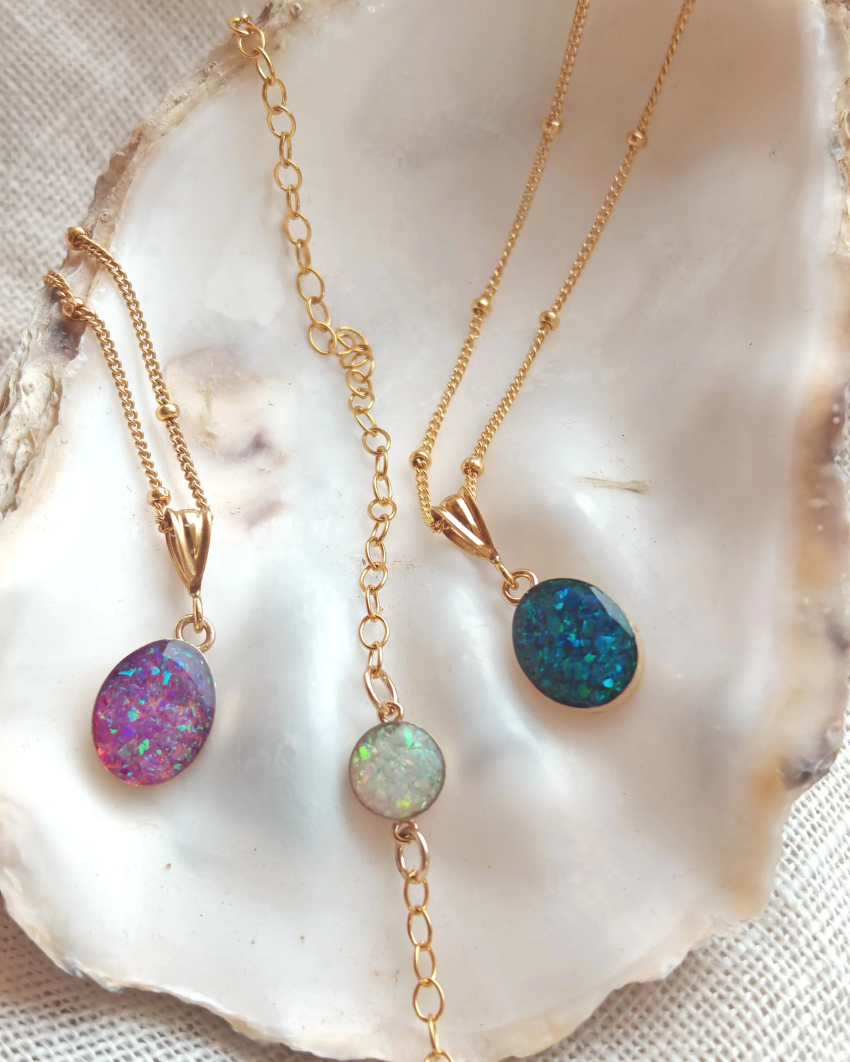 Gold necklaces with colorful gemstone pendants displayed on a white shell.